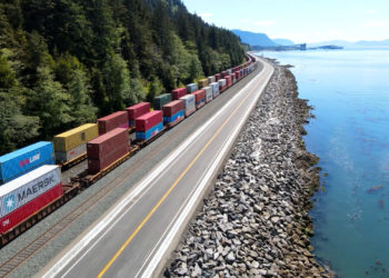 Cargo train with shipping containers moves along the coastline of British Columbia on its way through the Port of Prince Rupert